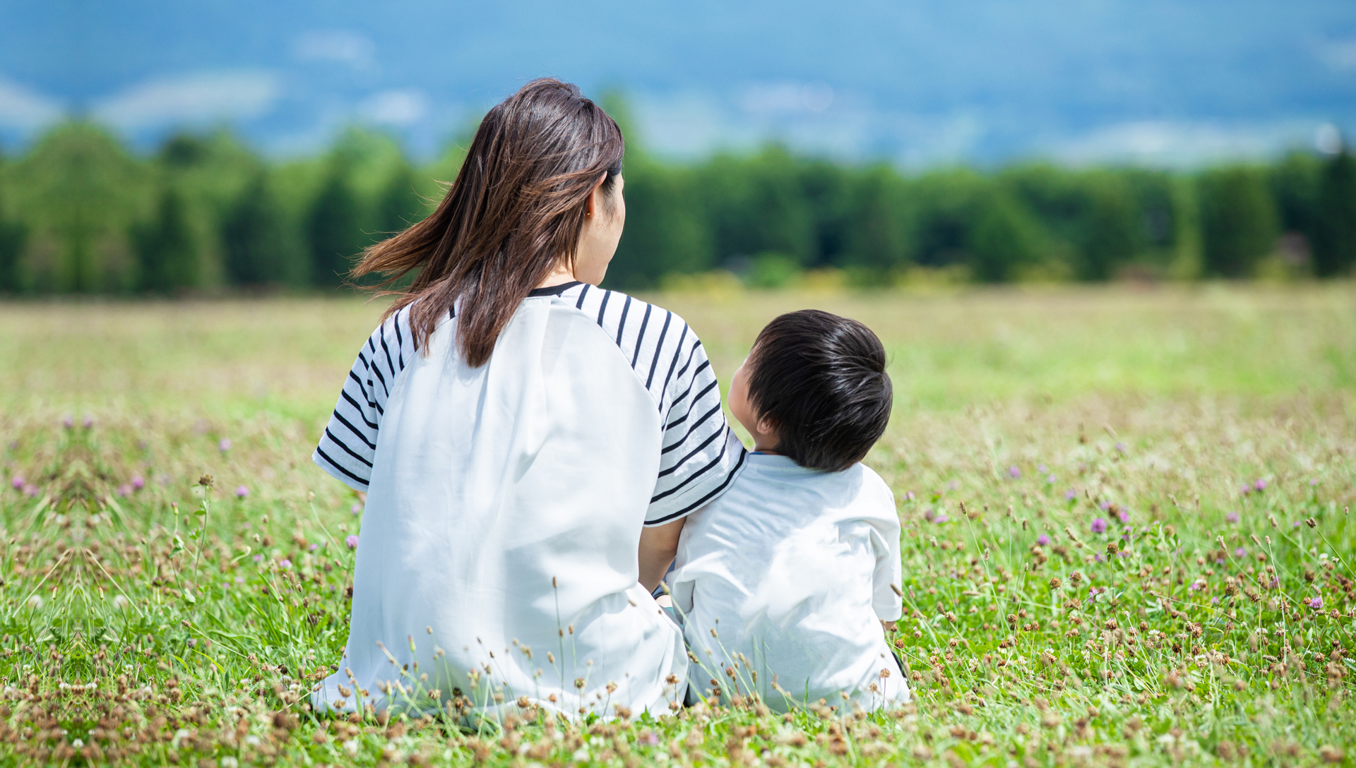 晴れた草原に並んで座っている母と男の子